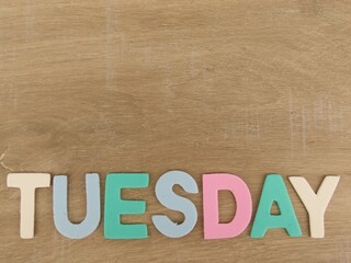 Multicolored eva foam letters form the word "Tuesday". Light wood background.