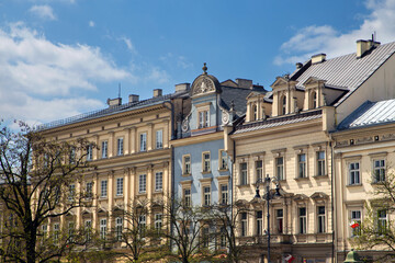 Fototapeta premium A vibrant row of historic townhouses lining the Market Square in Krakow, Poland, under a partly cloudy blue sky.