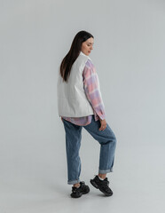 Portrait of a cute girl model in a pink checkered shirt and jeans in the studio on a white...
