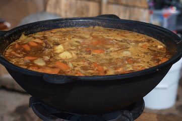 Cooking thick meat soup in a large cauldron outdoors. Catering concept. Chef stirs rich meat broth with vegetables. Close-up. Onion and carrot.