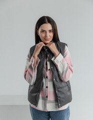 Portrait of a cute girl model in a pink checked shirt, vest and jeans in the studio on a white...