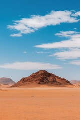 Naklejka premium A large rock formation sits in the middle of a desert. The sky is clear and blue, with a few clouds scattered throughout. The scene is peaceful and serene, with the only sounds being the wind
