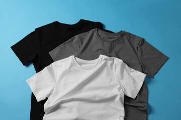 Blank t-shirts on light blue background, flat lay. Mockup for design