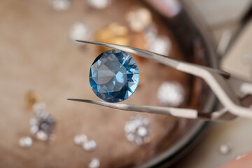 Tweezers with beautiful gemstone on blurred background, closeup
