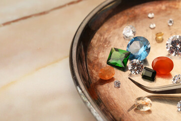 Tray with beautiful gemstones and tweezers on light table, closeup. Space for text