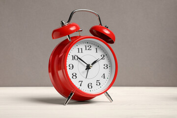 One red alarm clock on white wooden table against grey background