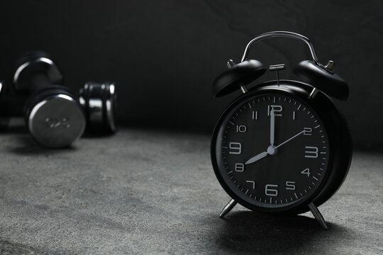 Alarm clock and dumbbells on grey background