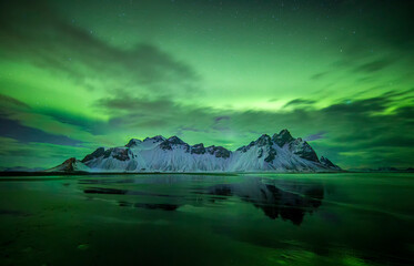 Vestrahorn reflected in the water in northen lights in Iceland