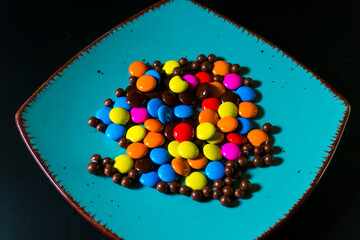 Close-up of colorful chocolate candies on a vibrant turquoise plate, perfect for food and confectionery themes