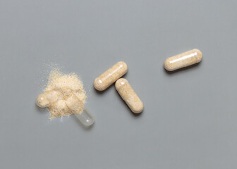Opened medical capsules to show beige powder on grey top view. Alternative dietary supplements