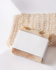 Beige handmade soap bar with blank label on soap saver bag on washbasin close up, mockup