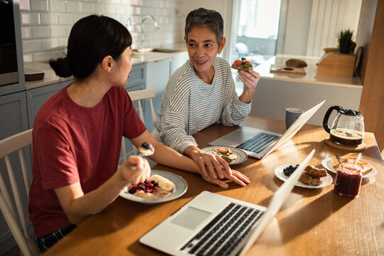 Lesbian couple having breakfast and working on laptops in kitchen