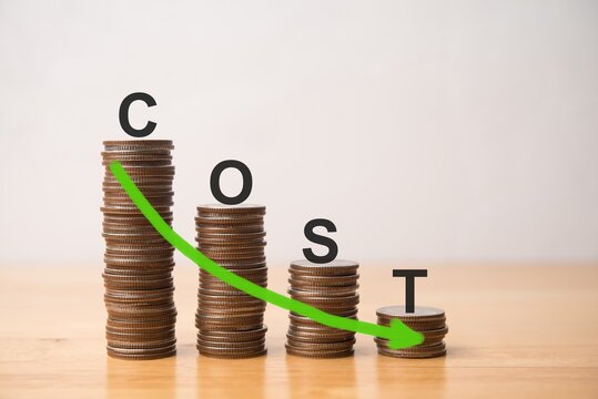 COST word and moving down arrow on decrease graph stack coins on wooden table with white wall background. Cost reduction, efficiency improvement, cost control and management concept.