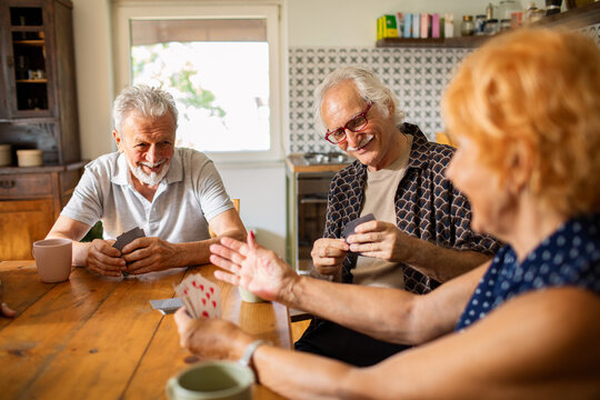 Senior friends playing cards together at kitchen table - Powered by Adobe