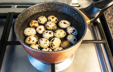 Top view of the gas stove in the kitchen, on which there is a sauce pan with granite walls, in which quail eggs are boiled in water.