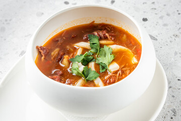 A delicious bowl of hearty soup featuring tender noodles, savory meat, bright red broth, and fresh herbs. Perfect for a comforting meal any time of the year.