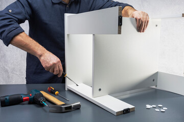 Handyman assembling furniture. Man using screwdriver for assembling shelf.