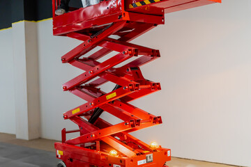 Red industrial hydraulic scissor lift extended with yellow warning sign bulbs. Small indoor space...
