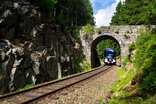 NEJDEK, CZECH REPUBLIC - JULY 23: Ceske drahy CD railway carrier company train passes under romantic stone bridge in beautiful forest in Ore Mountains on July 23, 2017 in Nejdek, Czech Republic.