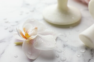 Orchid flower and spa stones on white marble table, closeup
