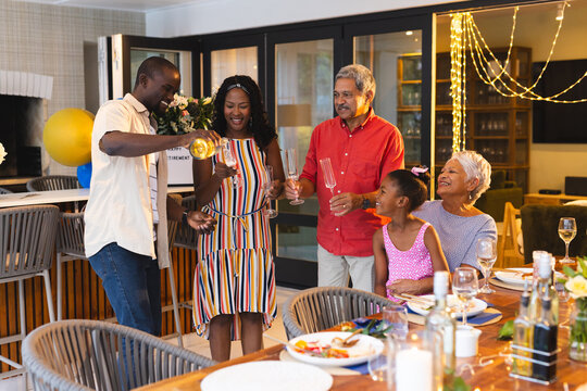 Multiracial family celebrating , enjoying drinks and laughter around dining table, in garden