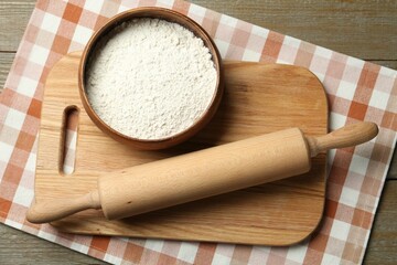 Rolling pin, bowl of flour and board on wooden table, top view