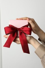 Woman holding gift box with beautiful bow against white wall, closeup