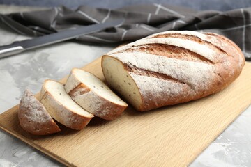 Wooden cutting board with fresh bread and knife on grey table, closeup