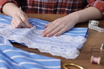 Woman sewing shirt with thread at wooden table, closeup