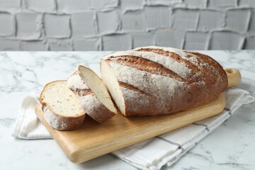 Wooden cutting board and loaf of bread on white marble table