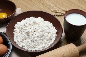 Rolling pin and ingredients for dough on wooden table, closeup
