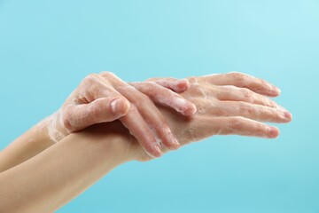 Fototapeta premium Woman washing hands with foaming soap on light blue background, closeup. Hygiene