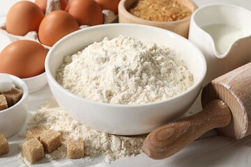 Rolling pin and ingredients for dough on white wooden table, closeup