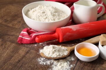 Rolling pin and ingredients for dough on wooden table, closeup