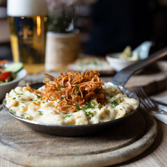 Traditionelle Käsespätzle mit knusprigen Röstzwiebeln, serviert in Gusseisenpfanne im Wirtshaus,...
