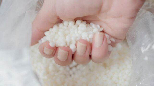 Close-up image of a hand holding small Soy wax white granules, commonly representing raw materials used in manufacturing, such as polymers or other industrial applications. Ideal for illustrating prod