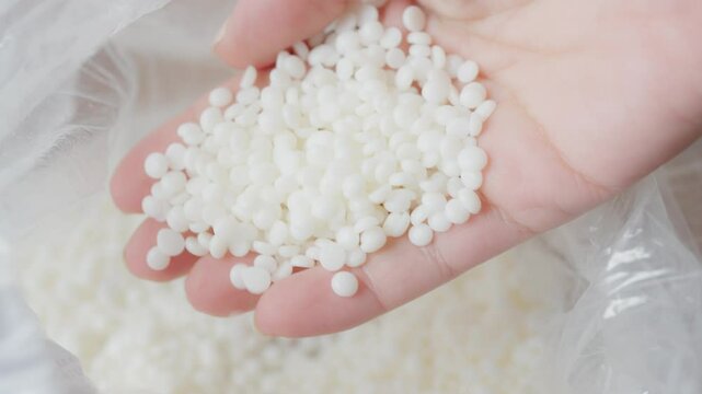 Close-up image of a hand holding small Soy wax white granules, commonly representing raw materials used in manufacturing, such as polymers or other industrial applications. Ideal for illustrating prod