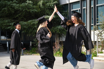 Two graduates in caps and gowns high fiving joyfully outside