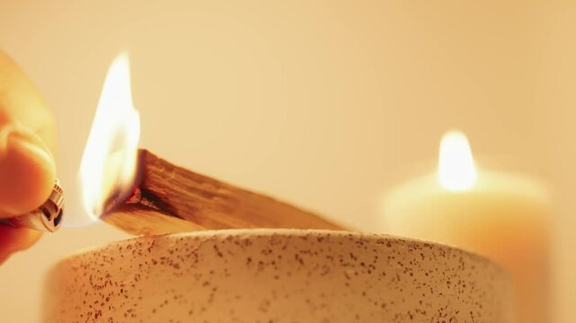A glowing burning palo santo stick rests on a ceramic holder, with soft candlelight radiating warmth, creating a serene and calming ambiance perfect for relaxation, meditation, or spiritual practices.