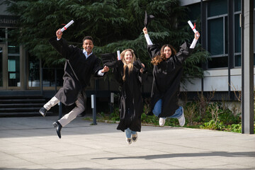 Group of cheerful graduates celebrating their graduation by joyfully jumping outdoors