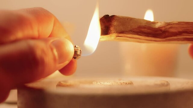 A close-up view of hands lighting a Palo Santo stick using a lighter, surrounded by calm candlelight. This serene image conveys a sense of mindfulness and peacefulness, ideal for wellness themes.