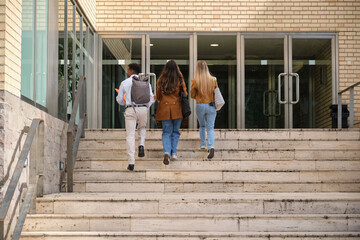 Group of diverse university students walking up the stairs to enter their college building