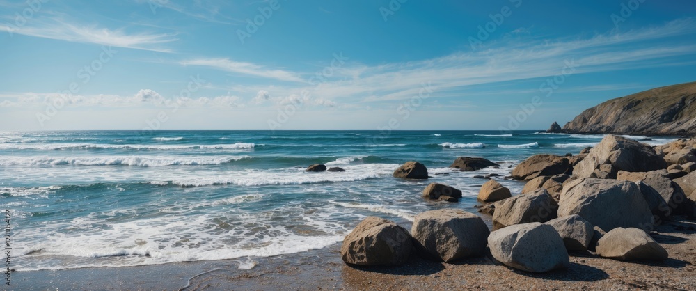 Sticker Rocky beach with waves lapping against the shore under a clear blue sky and distant hills in the background on a sunny day