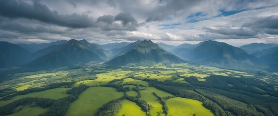 Aerial view of lush green fields and rugged mountains under a dramatic cloudy sky in a scenic landscape.