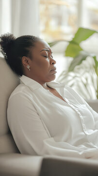Mature woman Black 40s sitting resting, eyes closed, home sofa peaceful escape worries stress, down time, soothing recovery recuperation, casual white shirt fashion