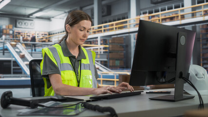 Caucasian Female Manager Checking Inventory On Desktop Computer In Warehouse Facility With Conveyor...