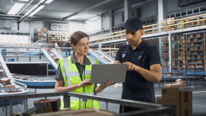 Distrubtion Fullfilment Center: Supervisor and Manager Talk, use Laptop Computer. Logistics and Transportation Warehouse Facility with Conveyor Loading Boxes with Products for Delivery to Clients.