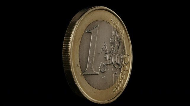 One euro coin spins around its axis on black background.