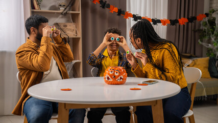 African american family of mom, dad and little son preparing for halloween celebrations, sitting at...