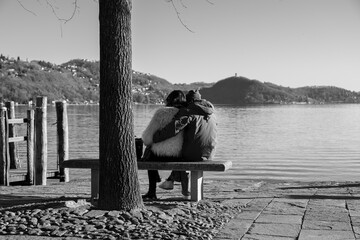 They look at the landscape.
A couple of friends admire the landscape on a bench. Subjects from behind. Black and white photo.